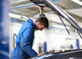 College mechanic student inspecting under car hood in repair garage