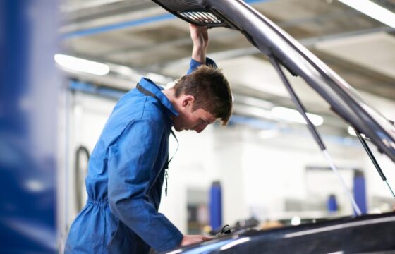 College mechanic student inspecting under car hood in repair garage