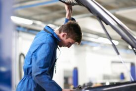 College mechanic student inspecting under car hood in repair garage